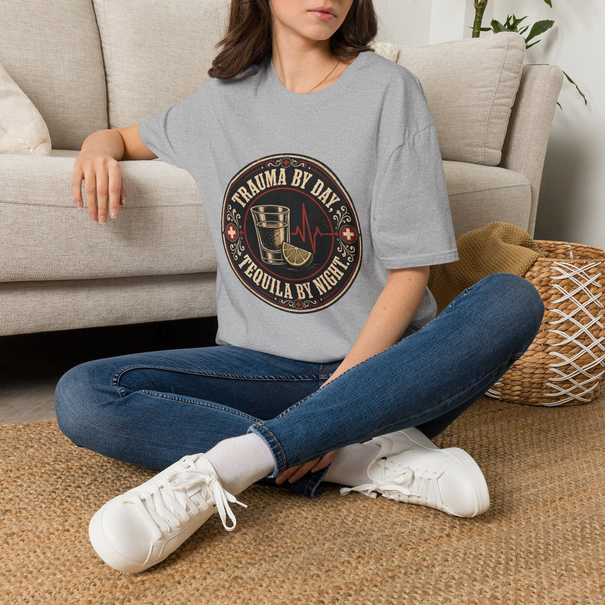 Trauma by Day, Tequila by Night Shirt, Sport Grey, worn by a model seated on the floor beside a sofa