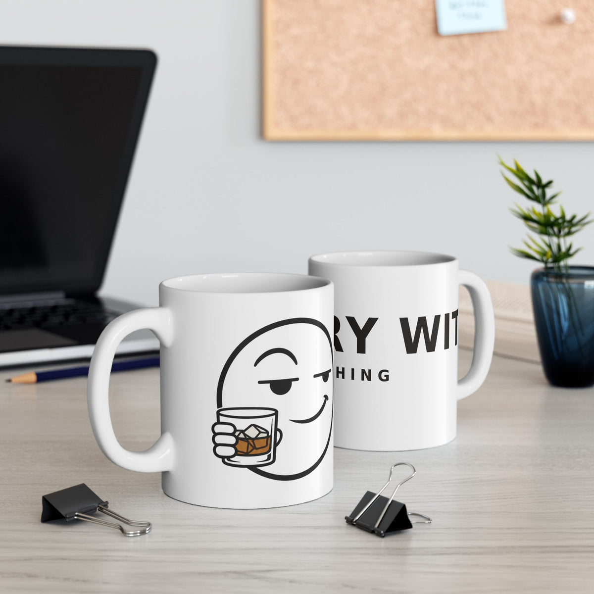 Dry Wit Logo Mug, white ceramic, lifestyle shot of two mugs on a desk beside a laptop, corkboard and small plant, showing both sides of the design