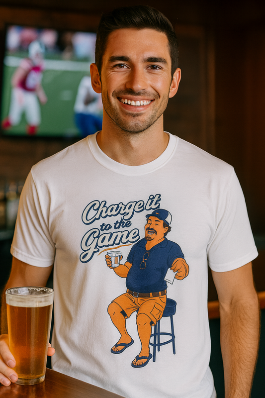 Smiling man in a white Charge It To The Game funny dad drinking shirt in a bar with football on TV behind him