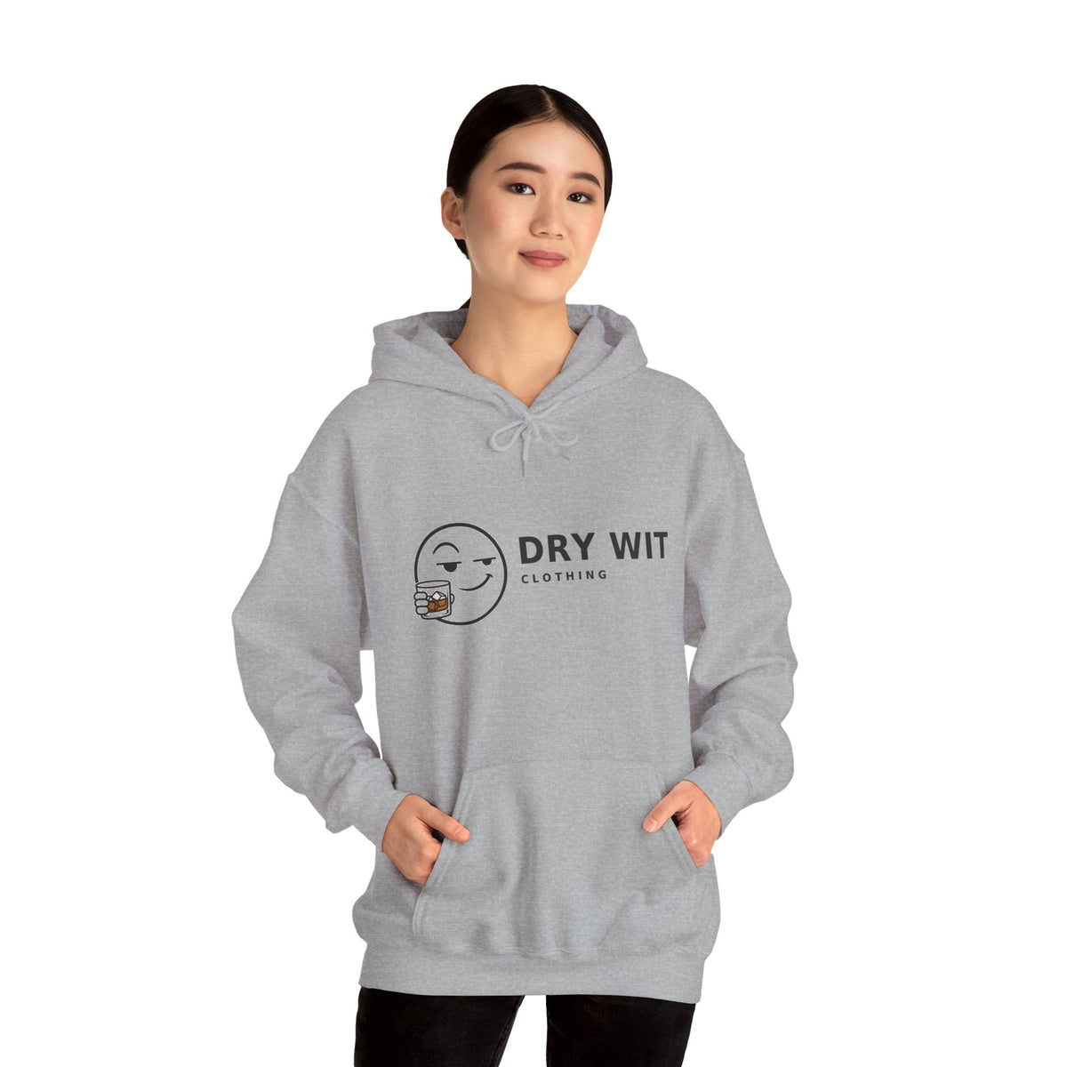Dry Wit Clothing logo hoodie with winking emoji holding a whiskey glass, Sport Grey, worn by a standing model with dark trousers, hands in the front pouch pocket