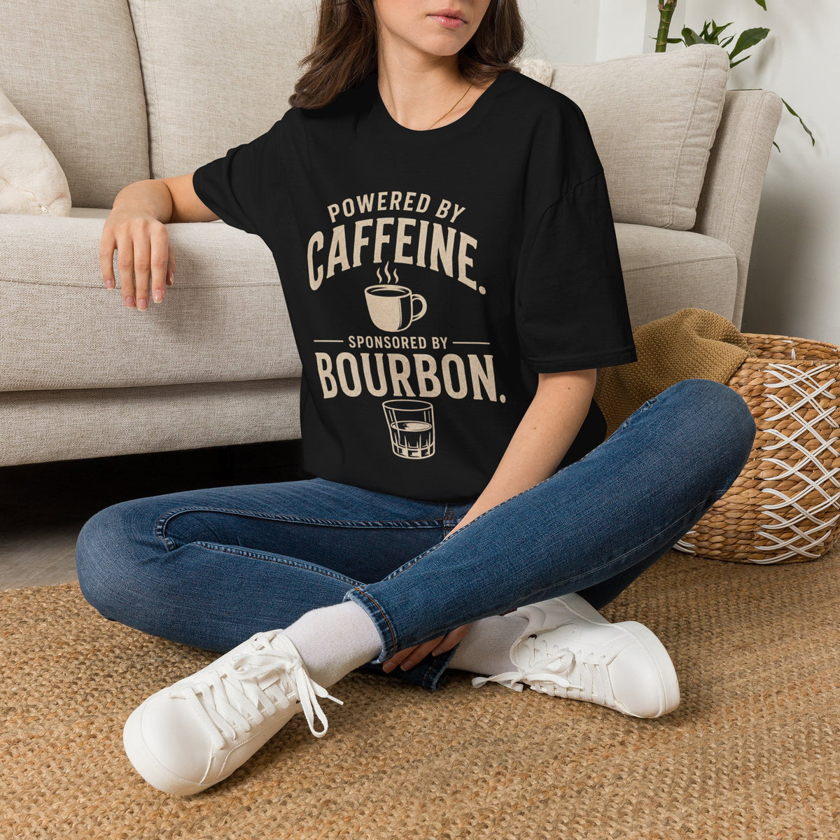 Powered by Caffeine Sponsored by Bourbon Shirt, Black, worn by a model seated on the floor beside a sofa