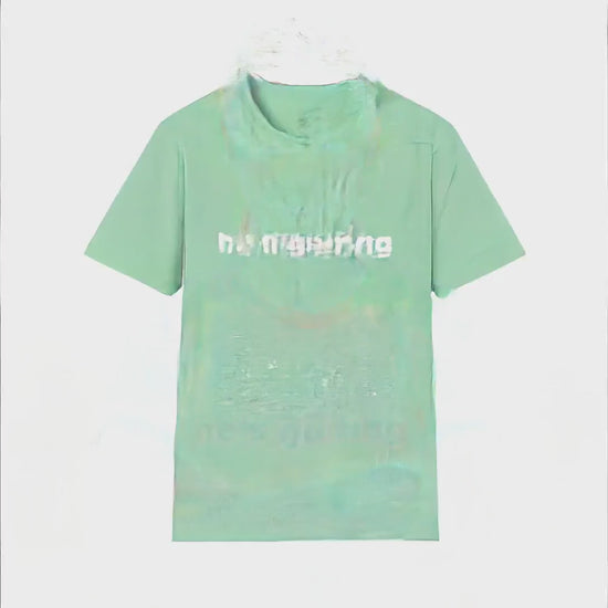 Video of a woman standing in a sunny driveway with arms crossed, giving an amused smirk toward the camera, wearing a mint green t-shirt with bold white text reading He's Golfing