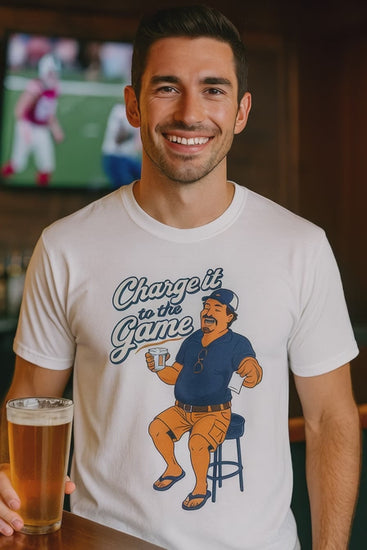 Video of a man in a white Charge It To The Game funny dad drinking shirt in a bar with football on TV behind him